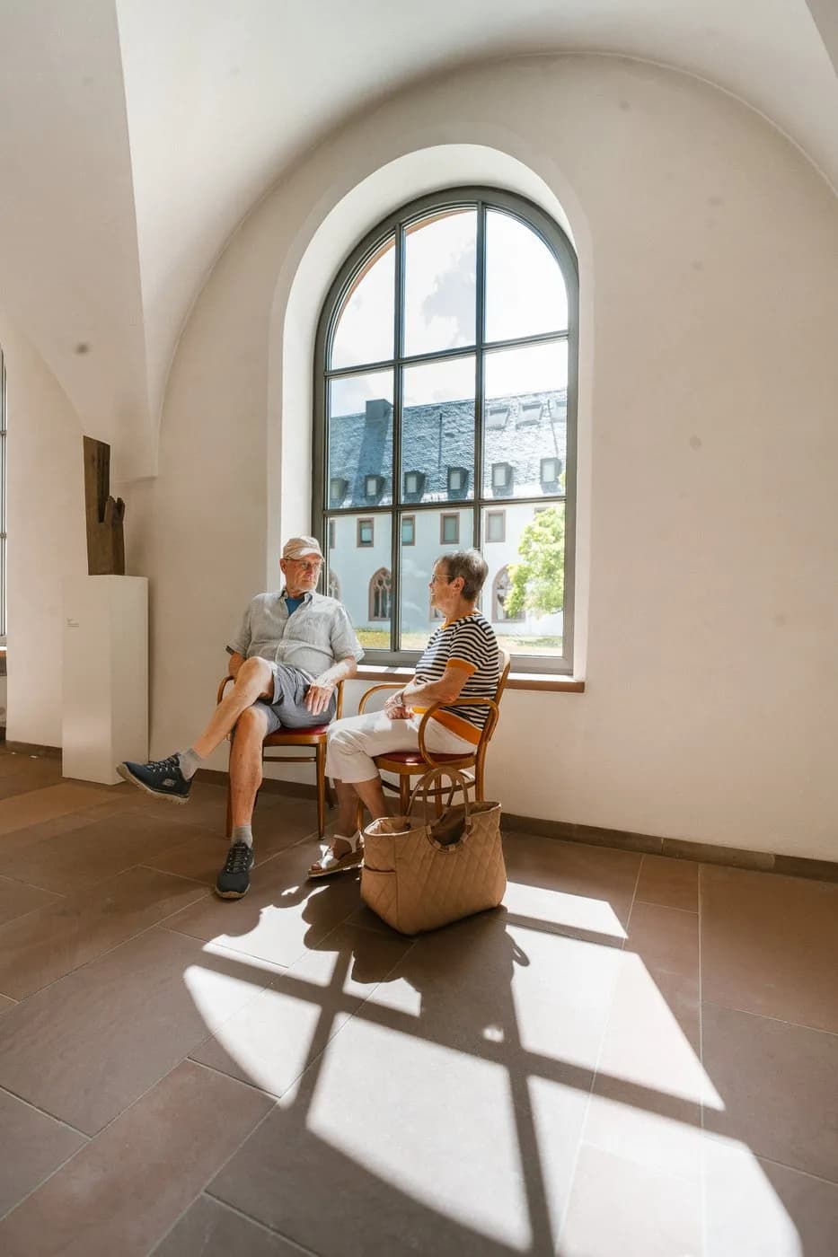 Ein Paar sitzt im hellen Gewölbegang am Fenster und unterhält sich, draußen der Innenhof